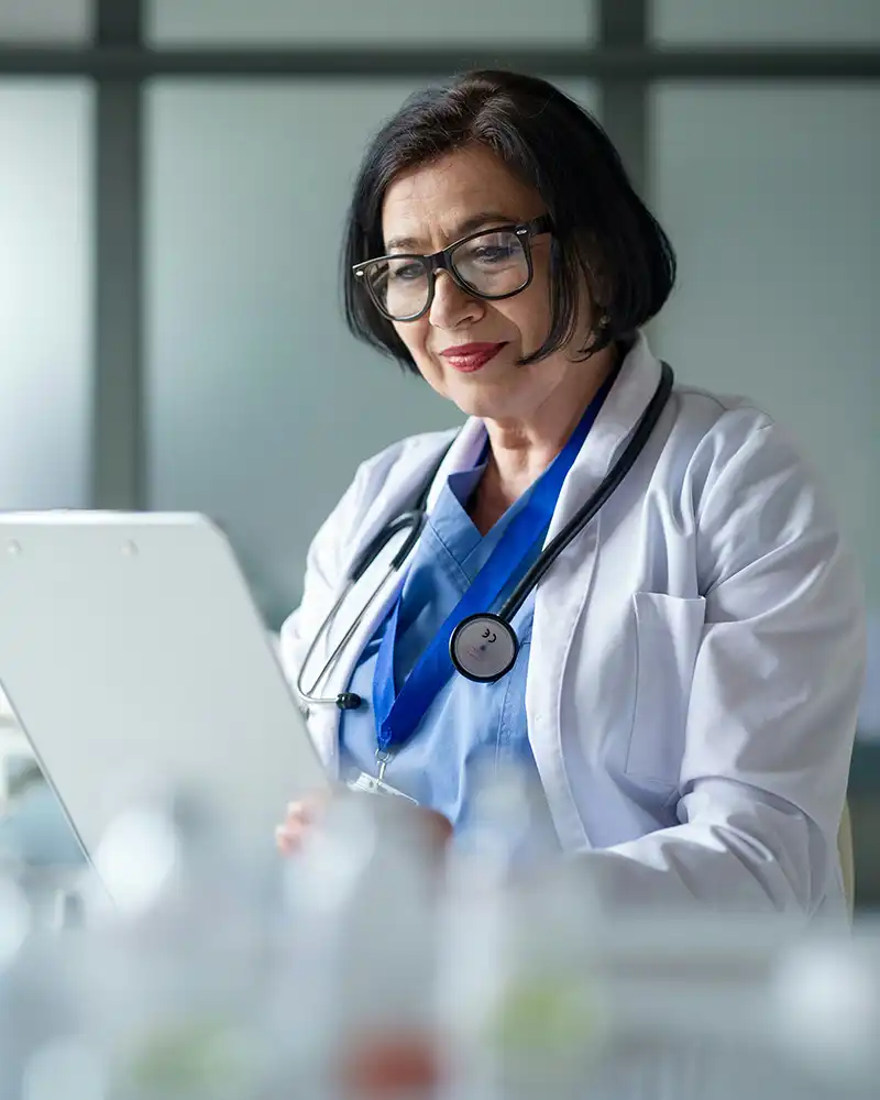 A female doctor with a stethoscope around her neck reading a patient's chart.