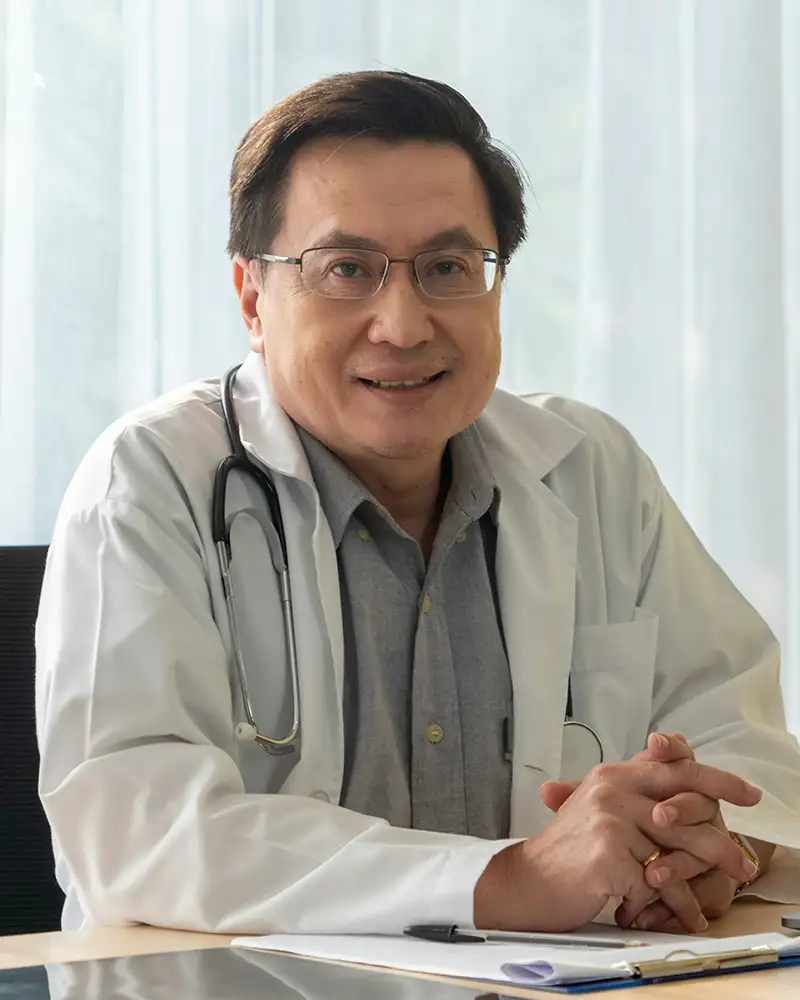 A male doctor in a lab coat with a stethoscope around his neck sitting at a desk.