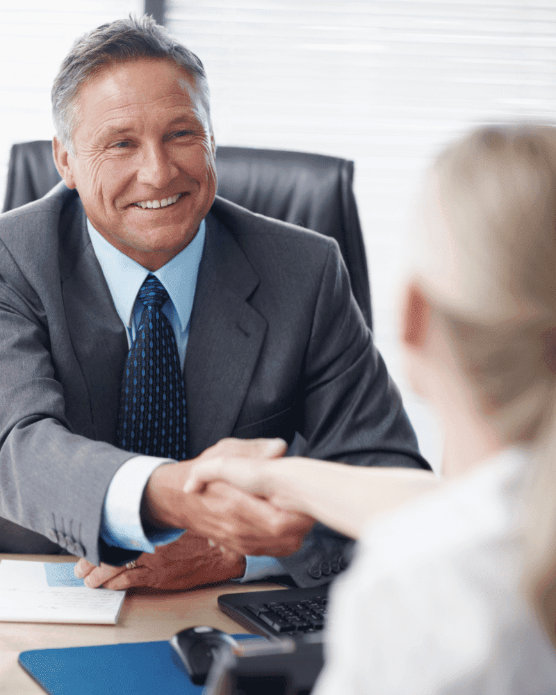 Financial advisor shaking hands with a female client in an office setting.
