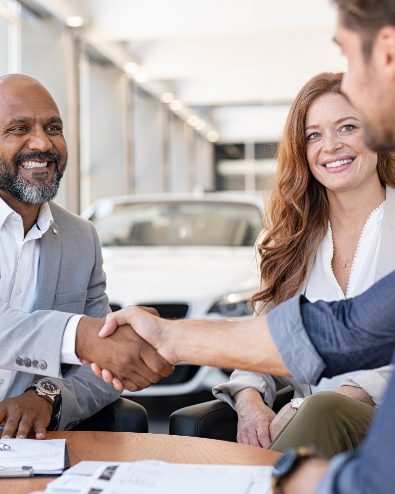 Sales associate shaking the hand of a new customer at a car dealership.