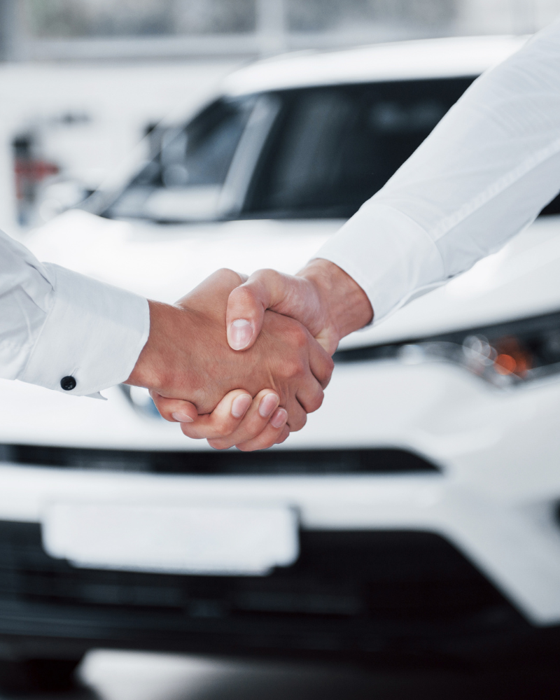 Two people shaking hands at a car dealership.